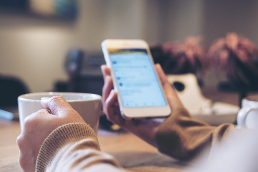 A woman's hands holding white coffee cup and mobile phone