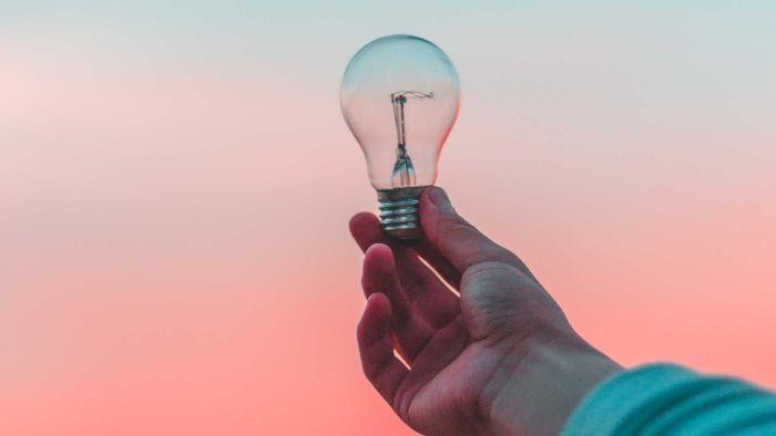 Person holding a lightbulb up to a evening sky