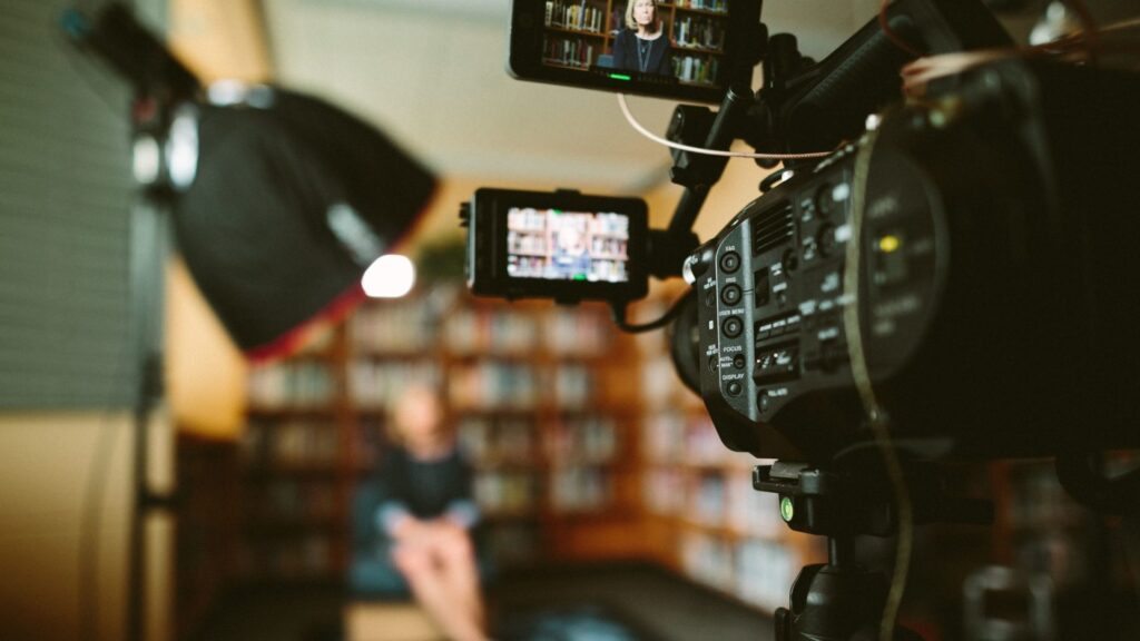 Close up of a in focus film cameras side monitor with a blurry room and woman sitting in the background