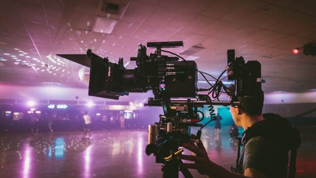 Sideview of a film camera with many attachments being operated by a man in a roller rink