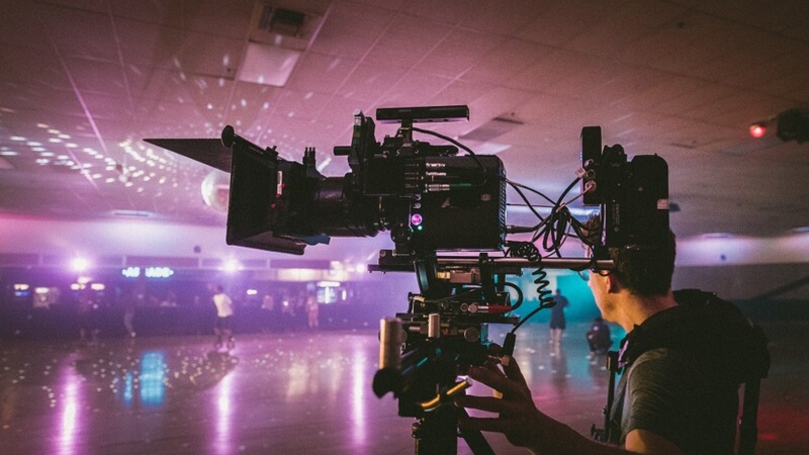 Sideview of a film camera with many attachments being operated by a man in a roller rink