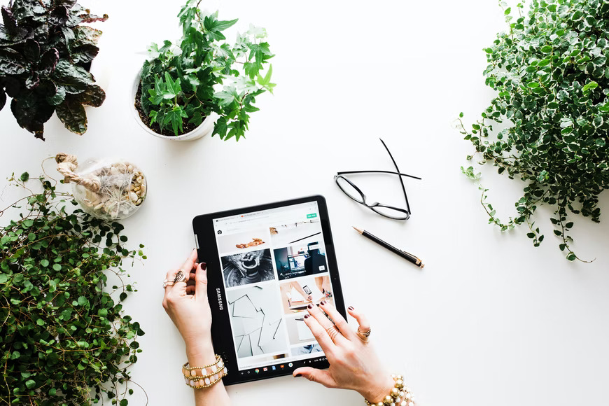 Woman looking at a tablet on a white table with glasses and plants