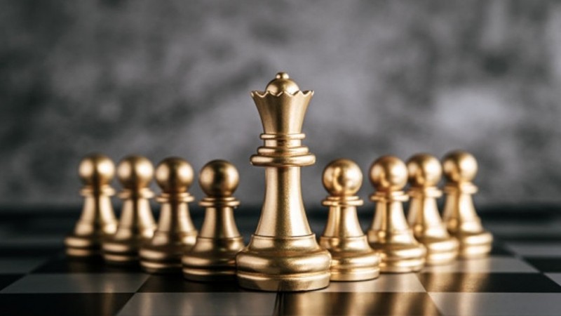 Gold queen and pawns chess pieces in a v formation on a board