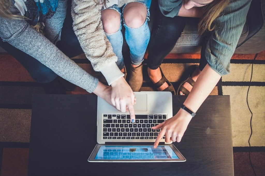 Aerial shot of 3 people pointing at the screen of a laptop on a small wooden table
