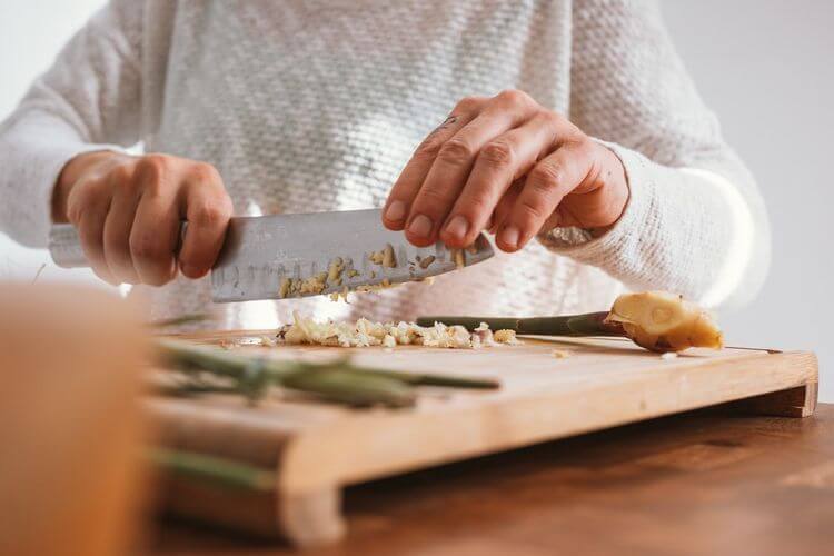 Person chopping garlic on a wooden cutting board