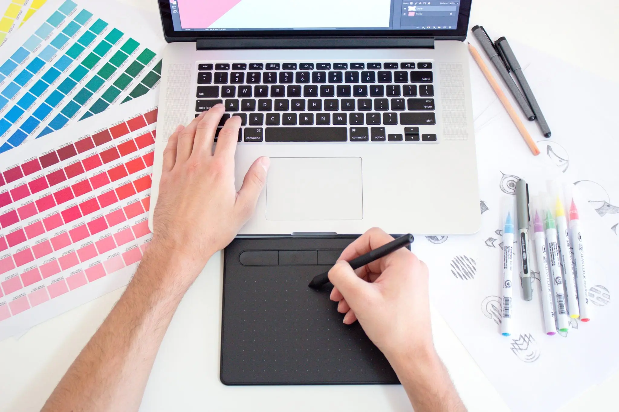 Person typing on a laptop with one hand while using a stylus on a stylus pad with the other