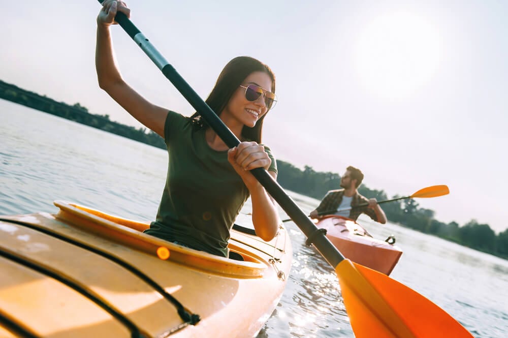 A woman an man kayaking in a river in orange kayaks and smiling