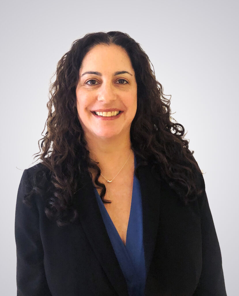 Professional headshot of a woman with black curly hair smiling wearing a black blazer with a blue shirt underneath on a white background