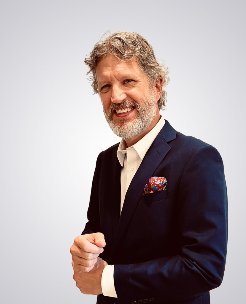 Professional headshot of a man with a beard smiling in a navy suit with a white dress shirt