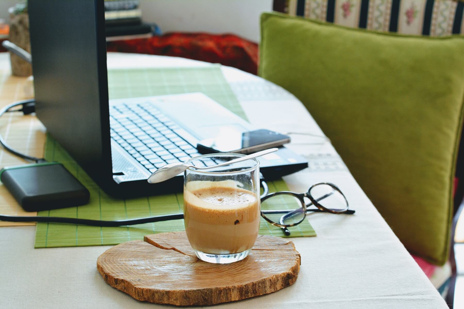A laptop, smartphone, glasses, and a coffee on a white table