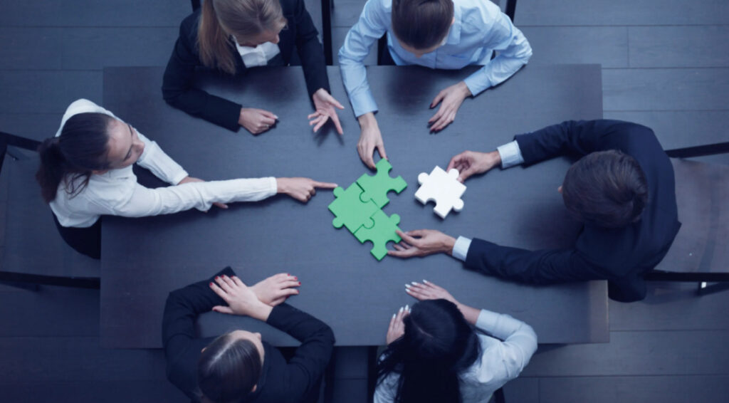 Aerial shot of 6 office workers solving a puzzle on the table in front of them