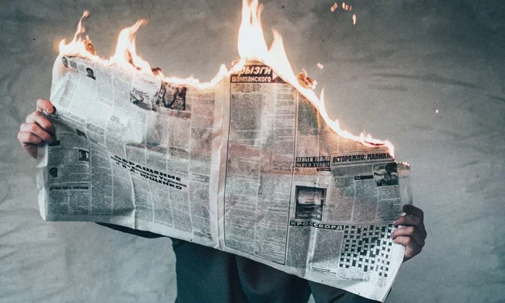 Person holding a newspaper that is being consumed by flames