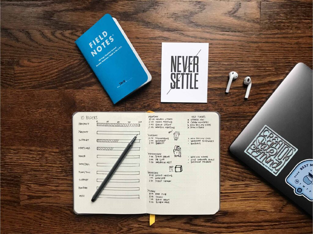 Wood table with note pads filled with organized notes, Apple airpods, and a laptop.