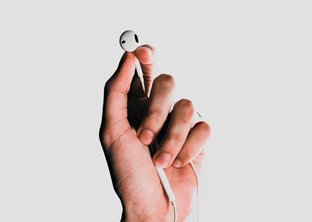 A left hand holding the left headphone for iPhones with a solid white background