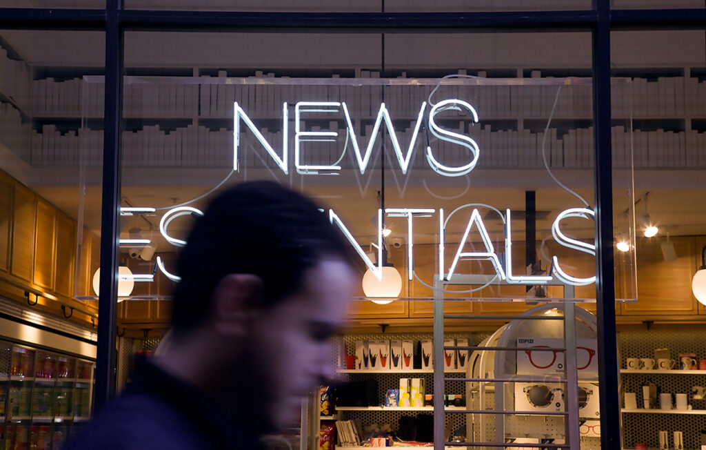The text "News essentials" formed by a white neon sign in a window