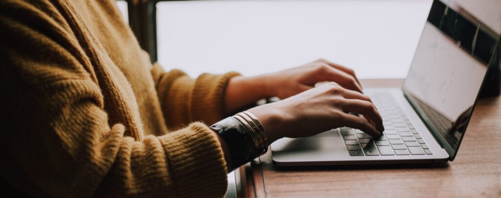 Sideview of a person typing on a laptop at wooden table
