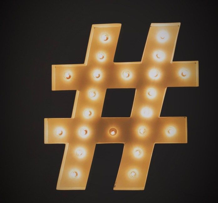 A yellow hashtag sign with lightbulbs on the outside in front of a black background