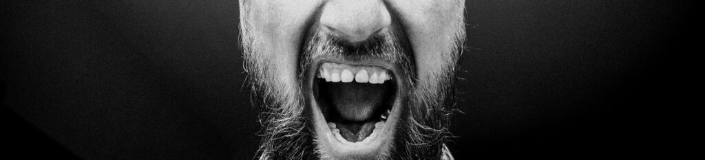 Black and white close up of a mans bearded screaming mouth