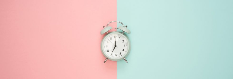An alarm clock on laying on a half pink and teal background