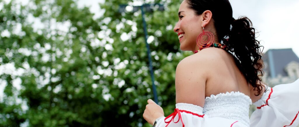 Black hair woman smiling and dancing in a white dress with red laces