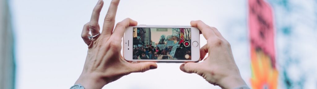 Close up of woman's hands holding an iPhone landscape recording a large group of people with signs