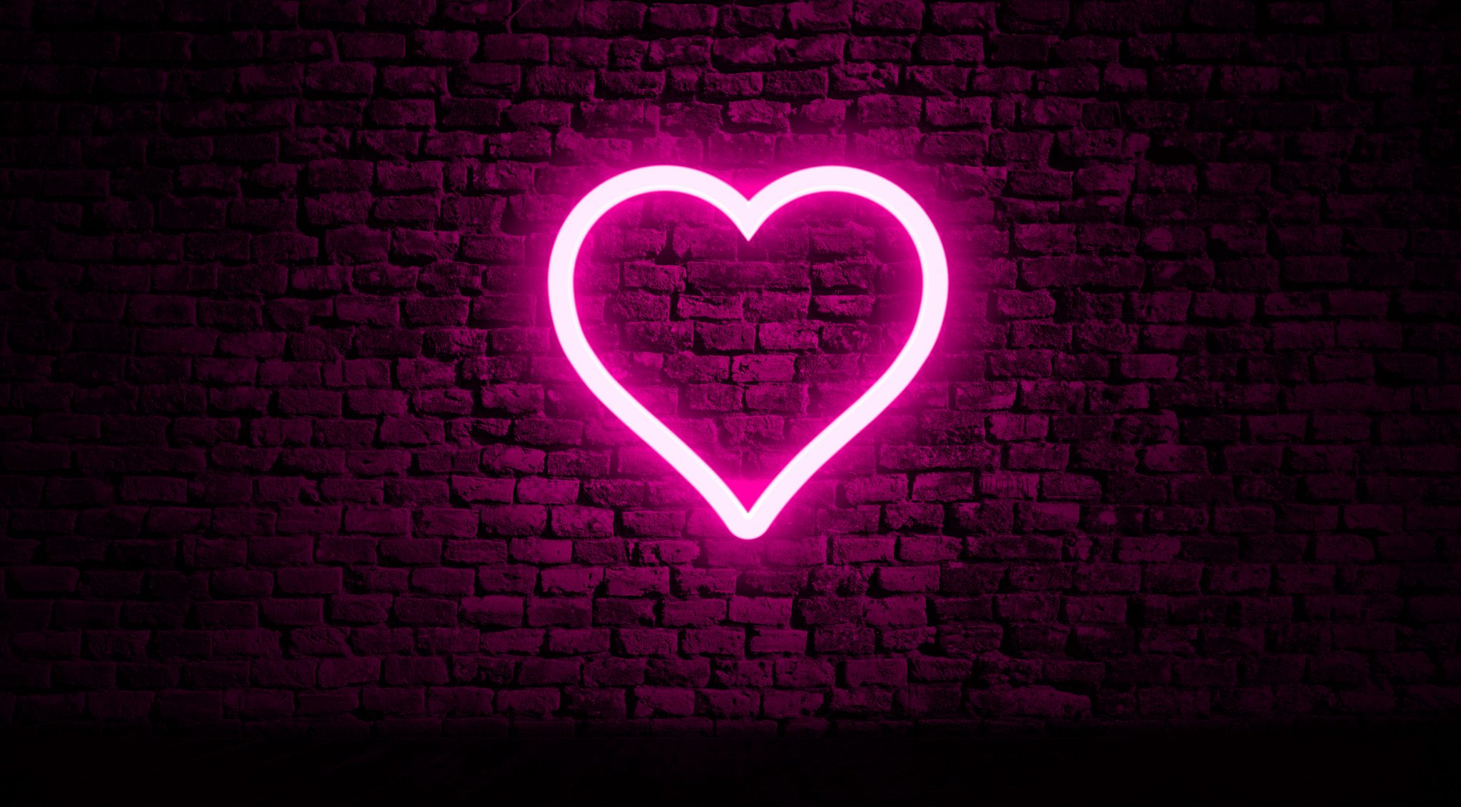 Pink neon heart illuminating a brick wall