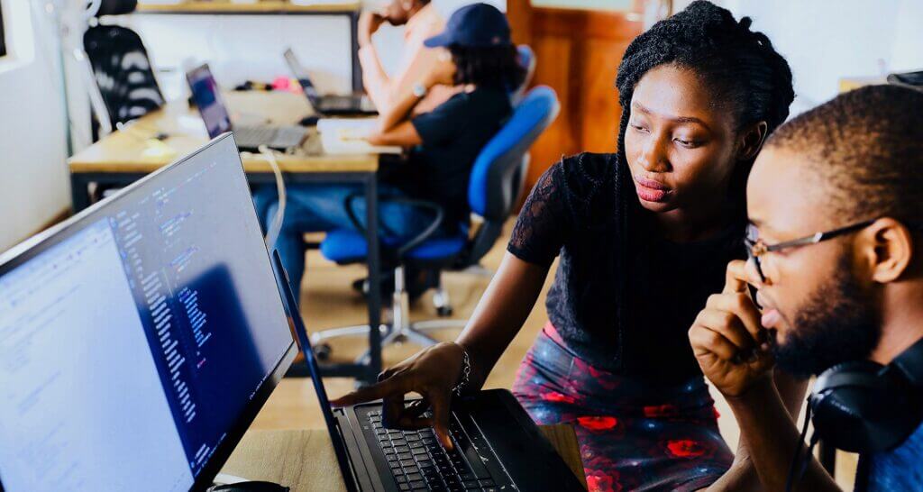Two people looking at a laptop and monitor screen