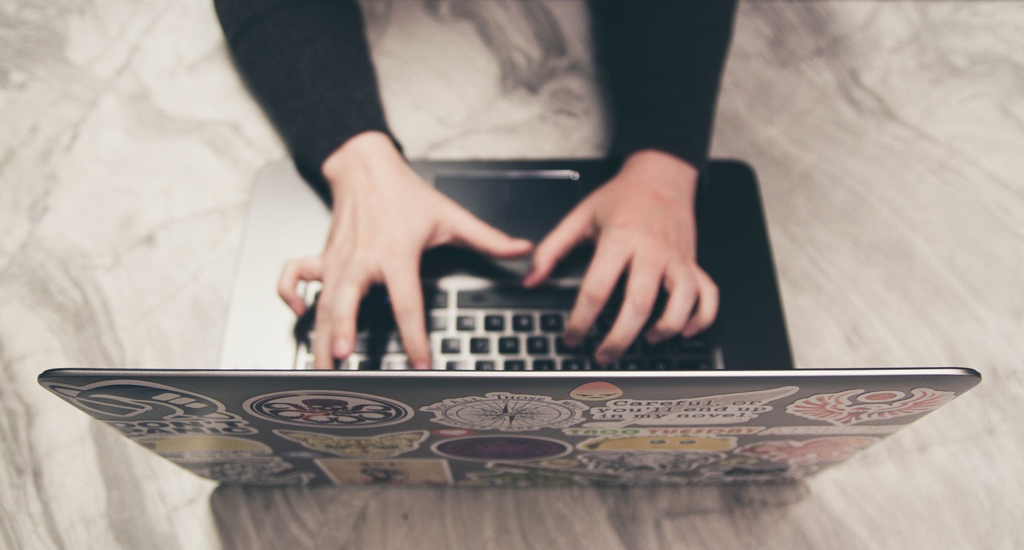 Aerial shot of a person typing on a laptop on a white and black marble counter