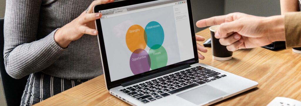 Person pointing at a laptop screen with 4 different color circles with the text "strengths", "Weaknesses", "Opportunities", "Threats".
