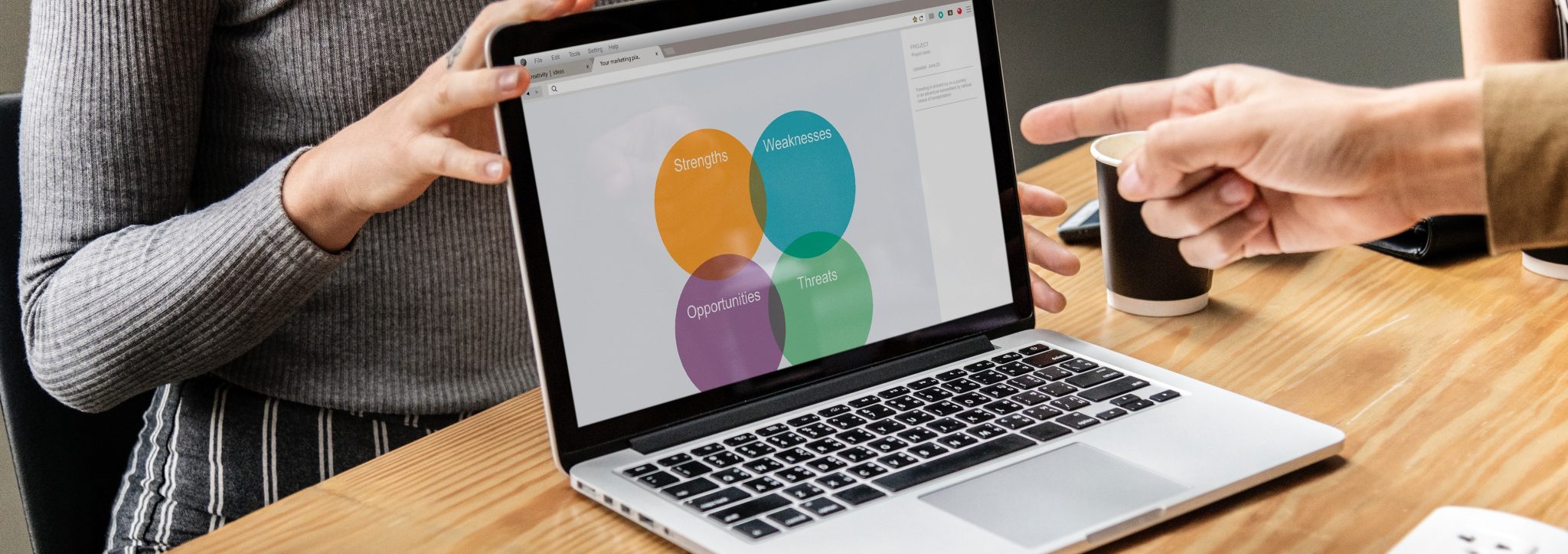 Person pointing at a laptop screen with 4 different color circles with the text "strengths", "Weaknesses", "Opportunities", "Threats".