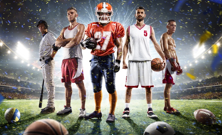 5 different sport athletes standing in an arc on a football field with 4 different sport balls on the ground