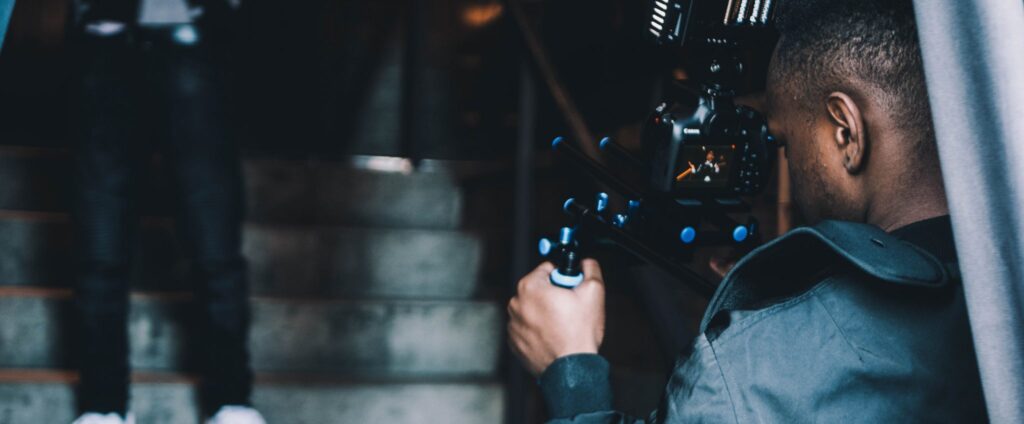 Man leaning with a film camera filming a person performing on a staircase