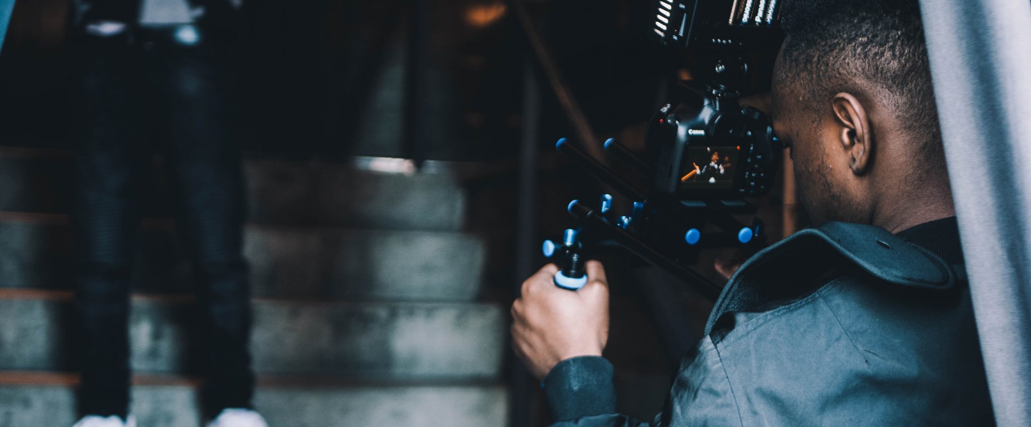 Man leaning with a film camera filming a person performing on a staircase