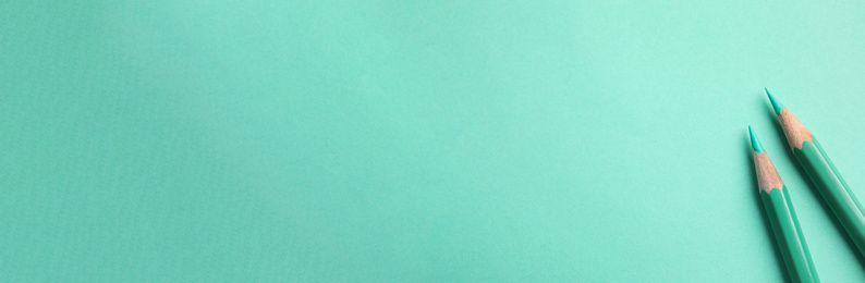 Two light green colored pencils laying on a similarly green background