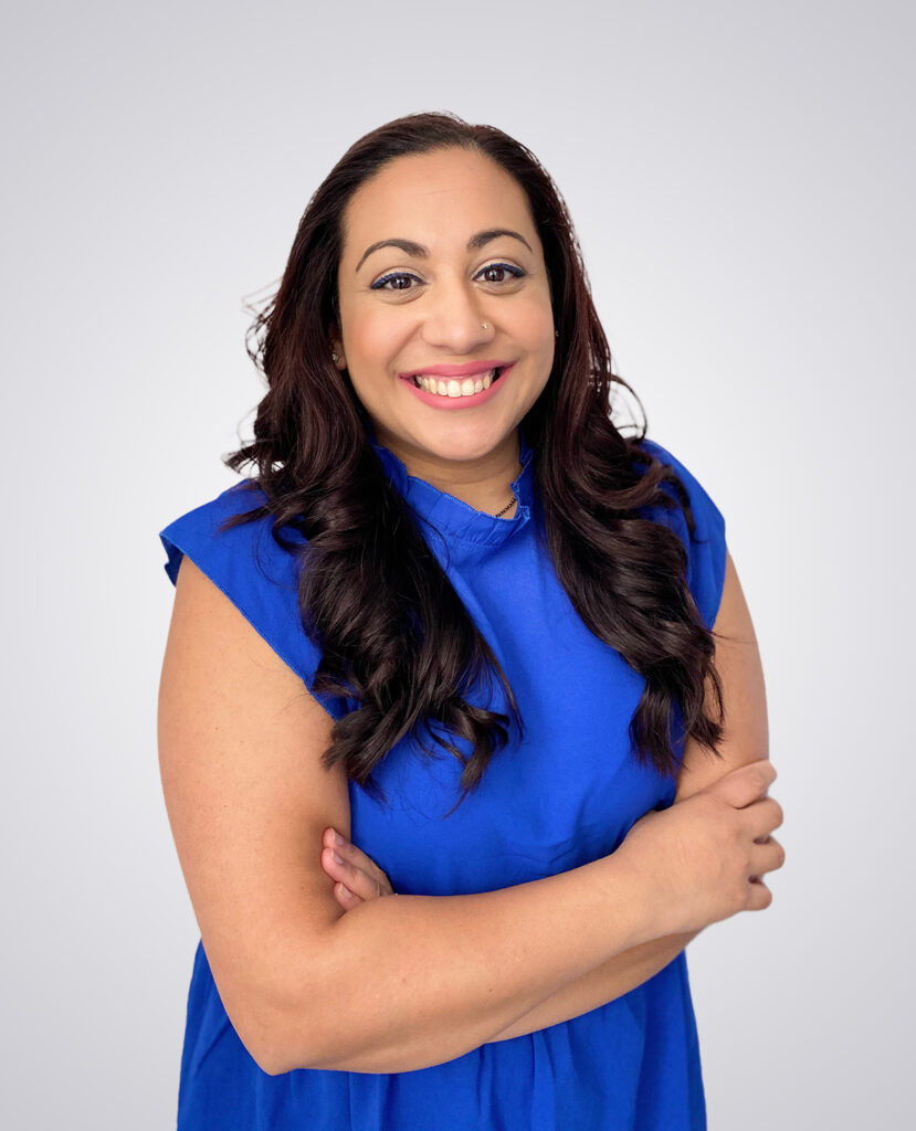 Professional headshot of a smiling woman with long brown hair in a blue dress on a white background