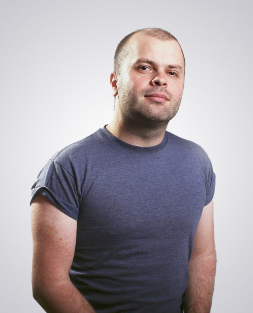 Professional headshot of a man smiling in a gray T-shirt on a white background