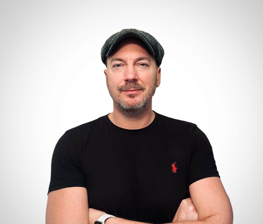 Smiling man in a black polo in front of a white background - Lee Kirton