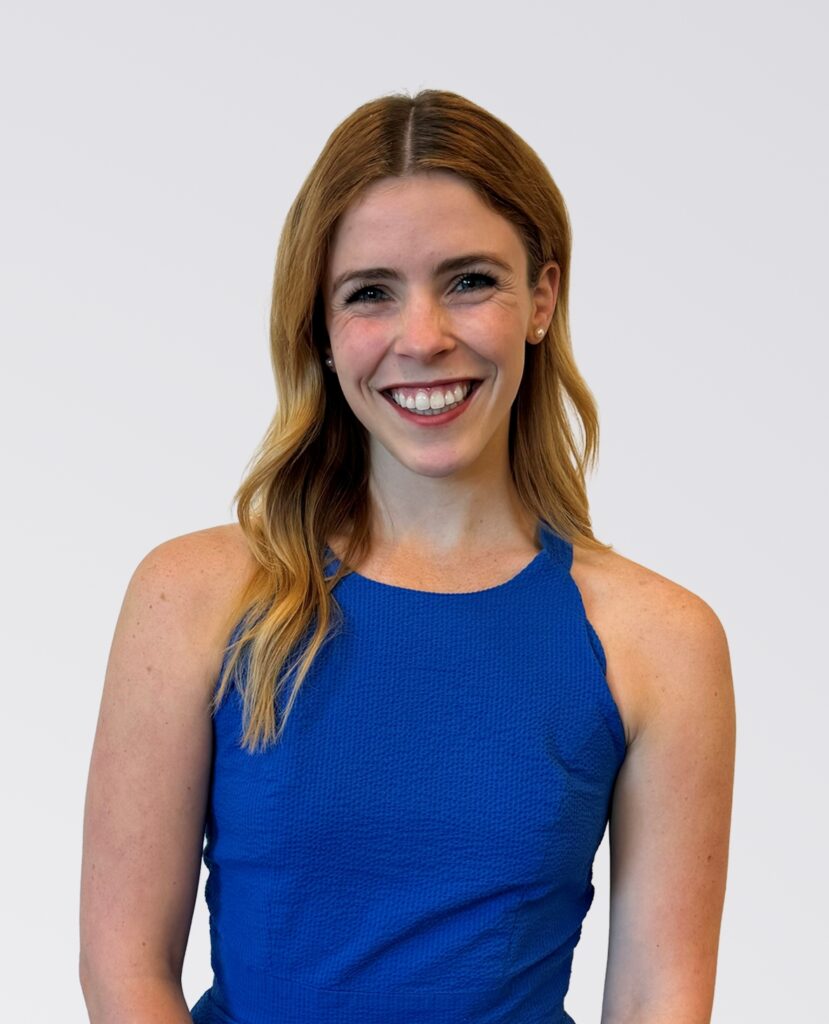 Professional headshot of smiling red haired woman in a blue dress - Rubie Darrow