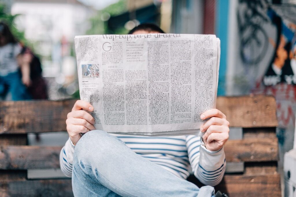 Man with legs crossed reading newspaper on a bench that is blockin his face
