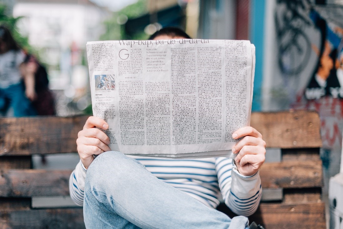 Man with legs crossed reading newspaper on a bench that is blockin his face