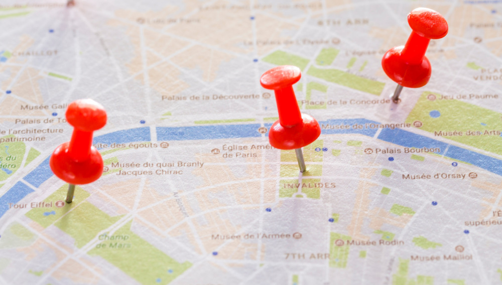 Close up of a paper map on a section of Paris, France with 4 red thumbtacks in sections of the map