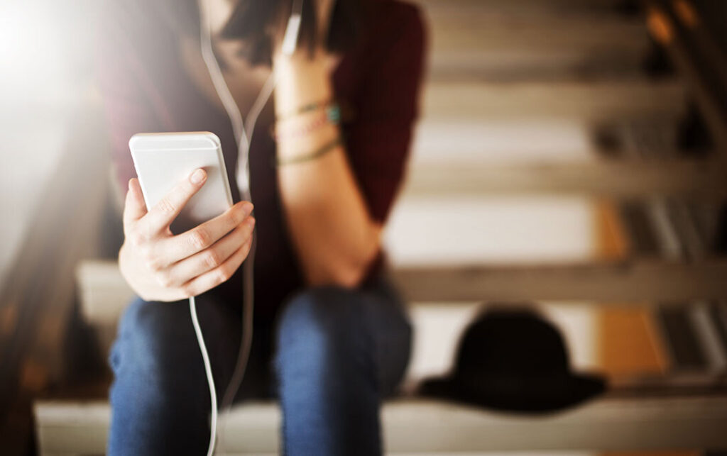 close up of a woman holding a phone with earphones in