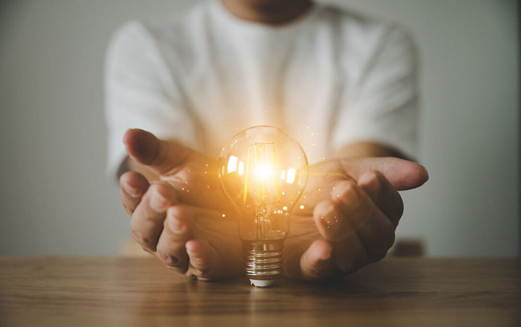 man putting his palms around an illuminating lightbulb on a wooden table
