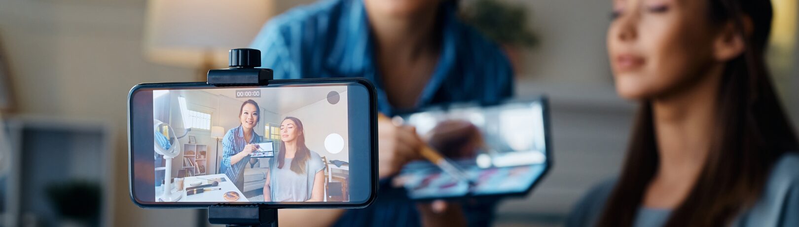 close up of a phone that is recording two women as one does the others makeup