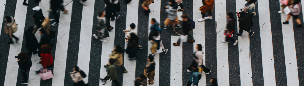 Aerial angle blurry image of many people walking across a white striped crossing section of a city road