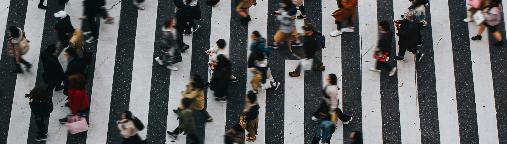 Aerial angle blurry image of many people walking across a white striped crossing section of a city road