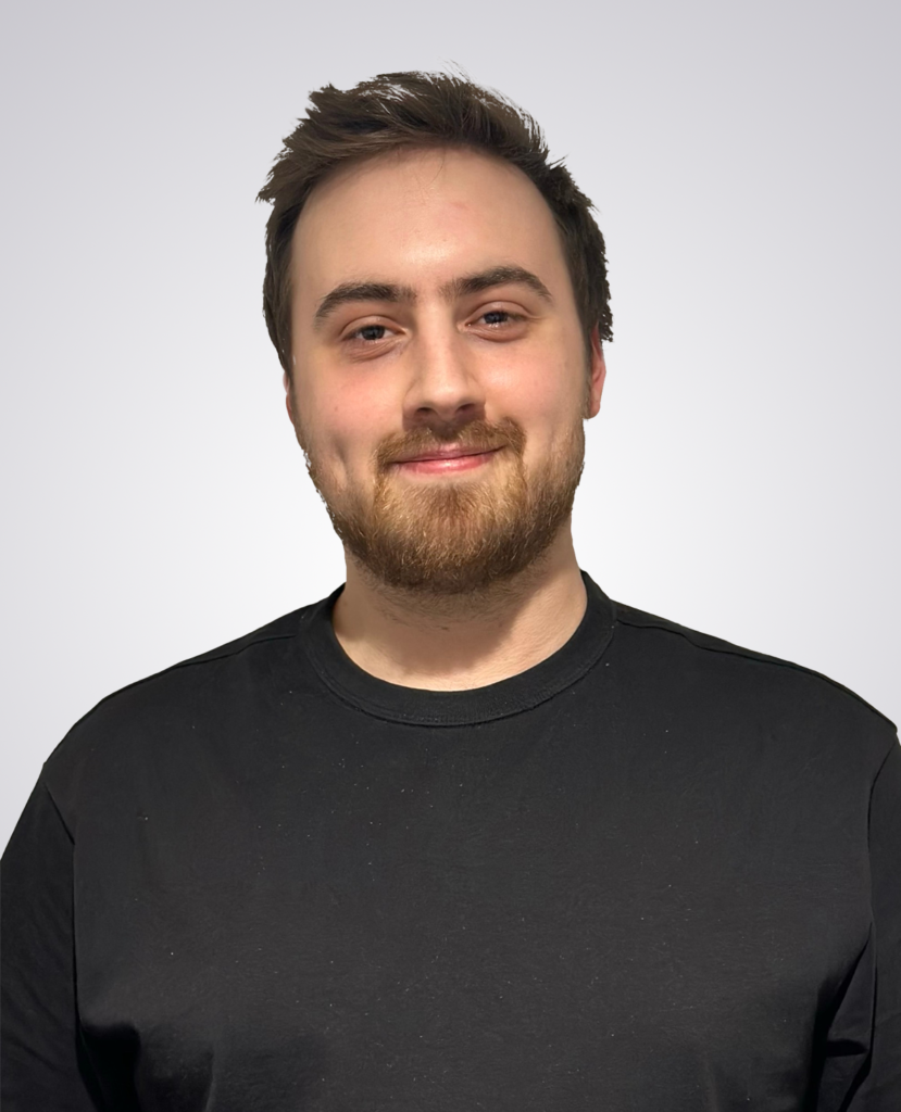 Professional headshot of a man with short brown hair smiling wearing a black t-shirt on a white background