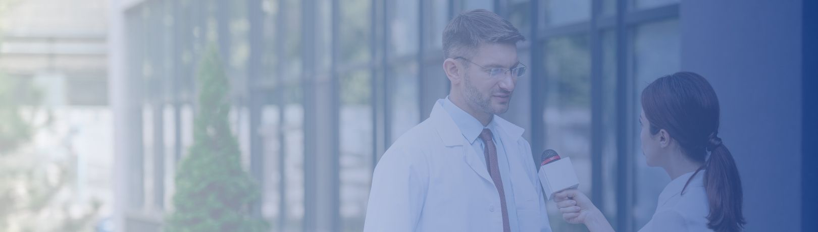 man in white lab coat with glasses being interviewed by woman with microphone