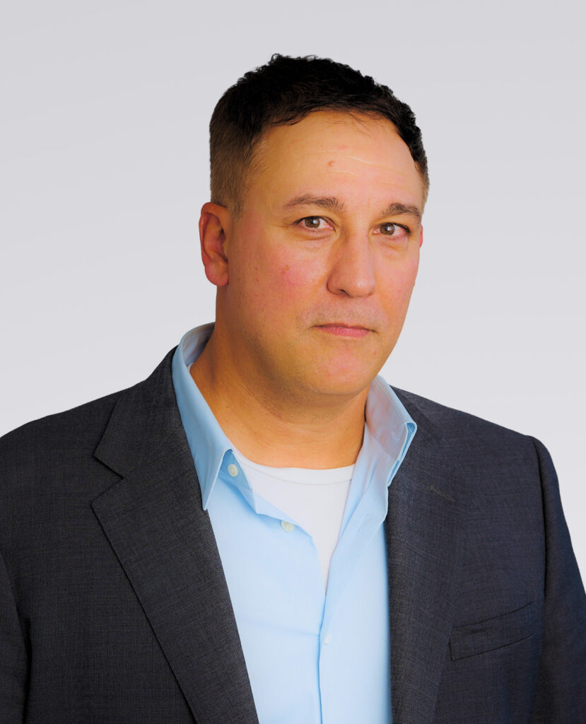 Professional headshot of man with brown hair wearing a navy blazer and magenta undershirt on a white background