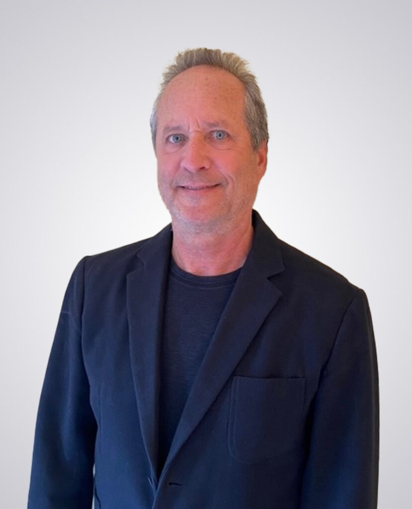 Professional headshot of a man smiling wearing a black blazer and black shirt underneath on a white background